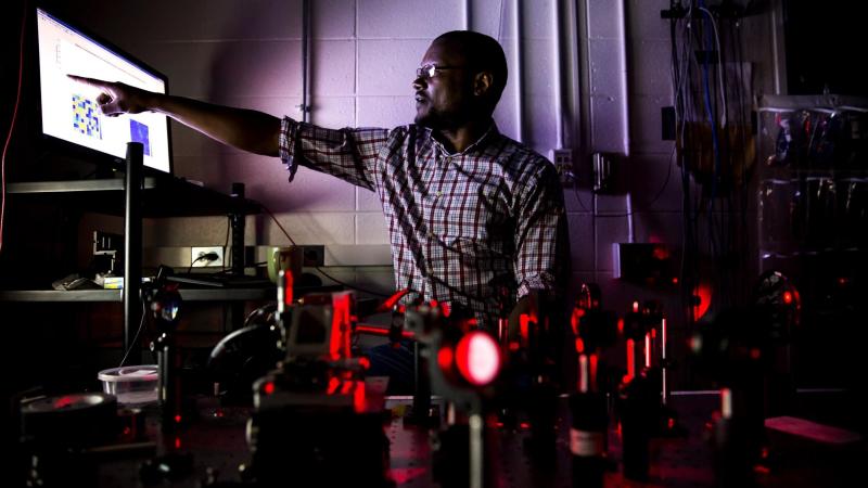 Professor in a dark room points at a bright monitor